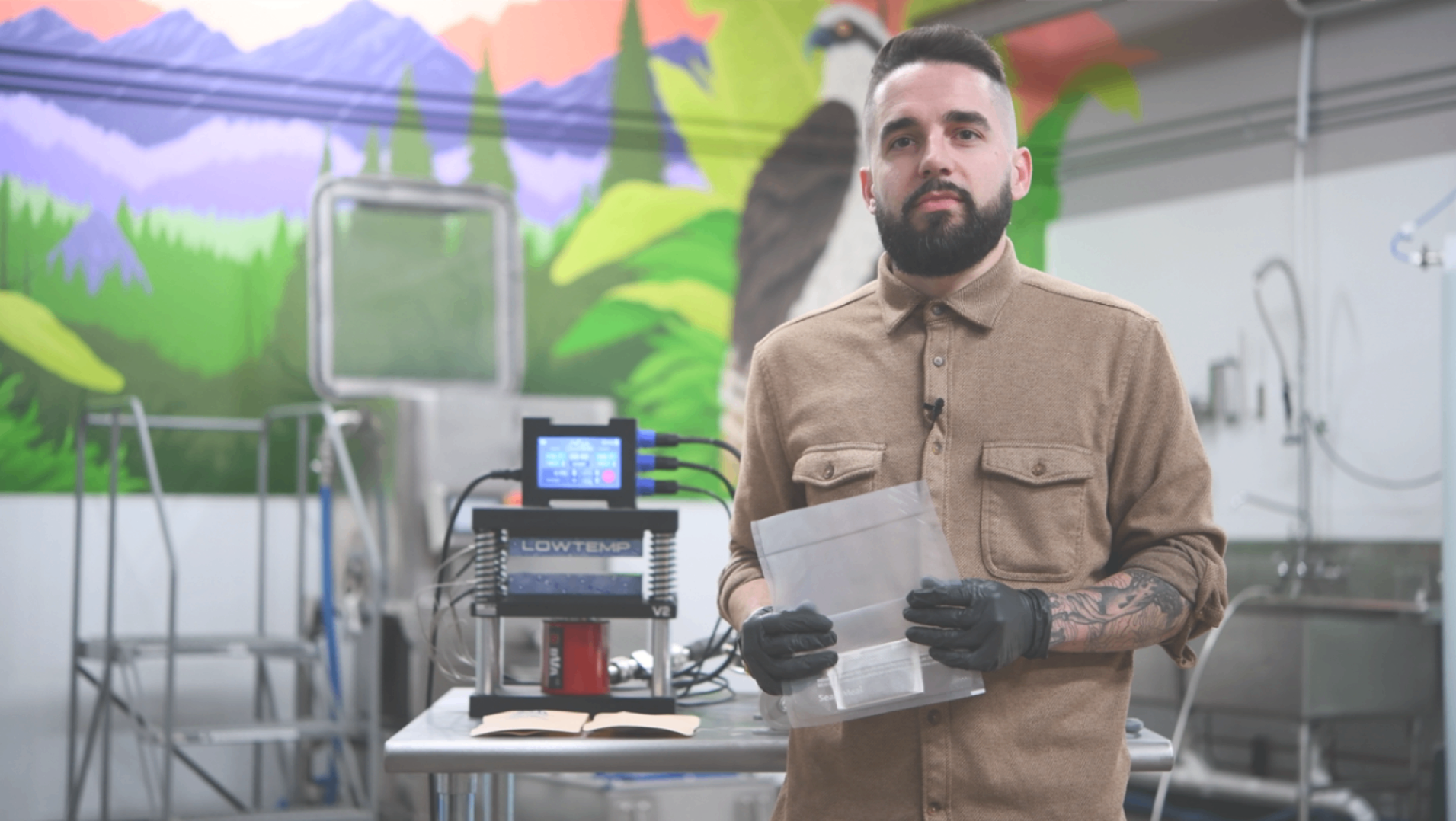 Cliff from Lowtemp Industries in the hash lab holding a wash bag with a V2 rosin press on the table
