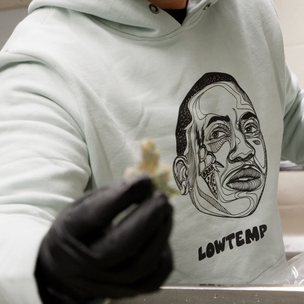 Person wearing a hoodie with a face design and 'LOWTEMP' text, holding a small object.