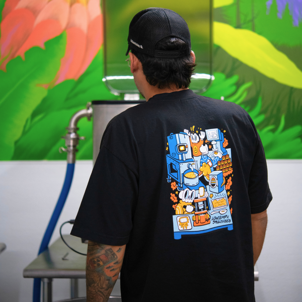 Person wearing a black t-shirt with colorful graphic design, standing in front of a colorful mural.