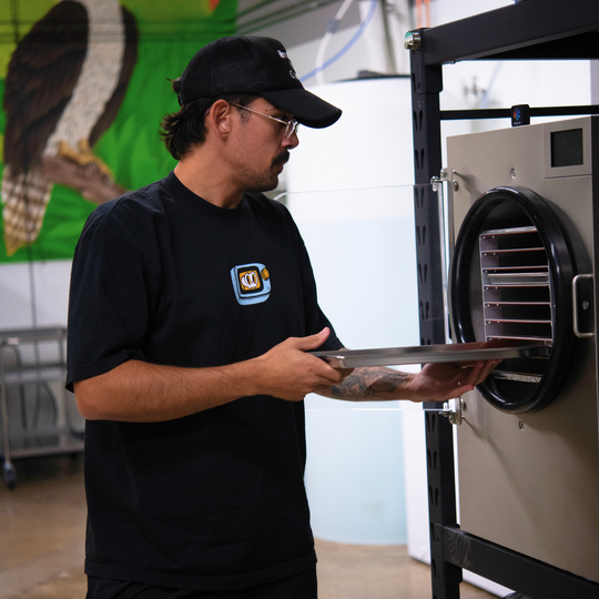 Person in a black shirt with a logo holding a tray of food in front of an industrial oven.