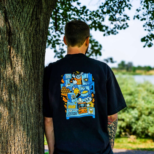 Person wearing a black t-shirt with colorful graphic design, standing against a tree outdoors.