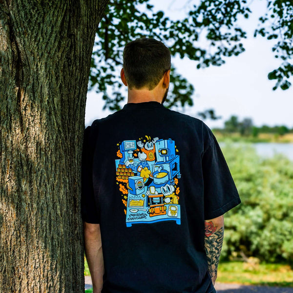 Person wearing a black t-shirt with colorful graphic design, standing against a tree outdoors.