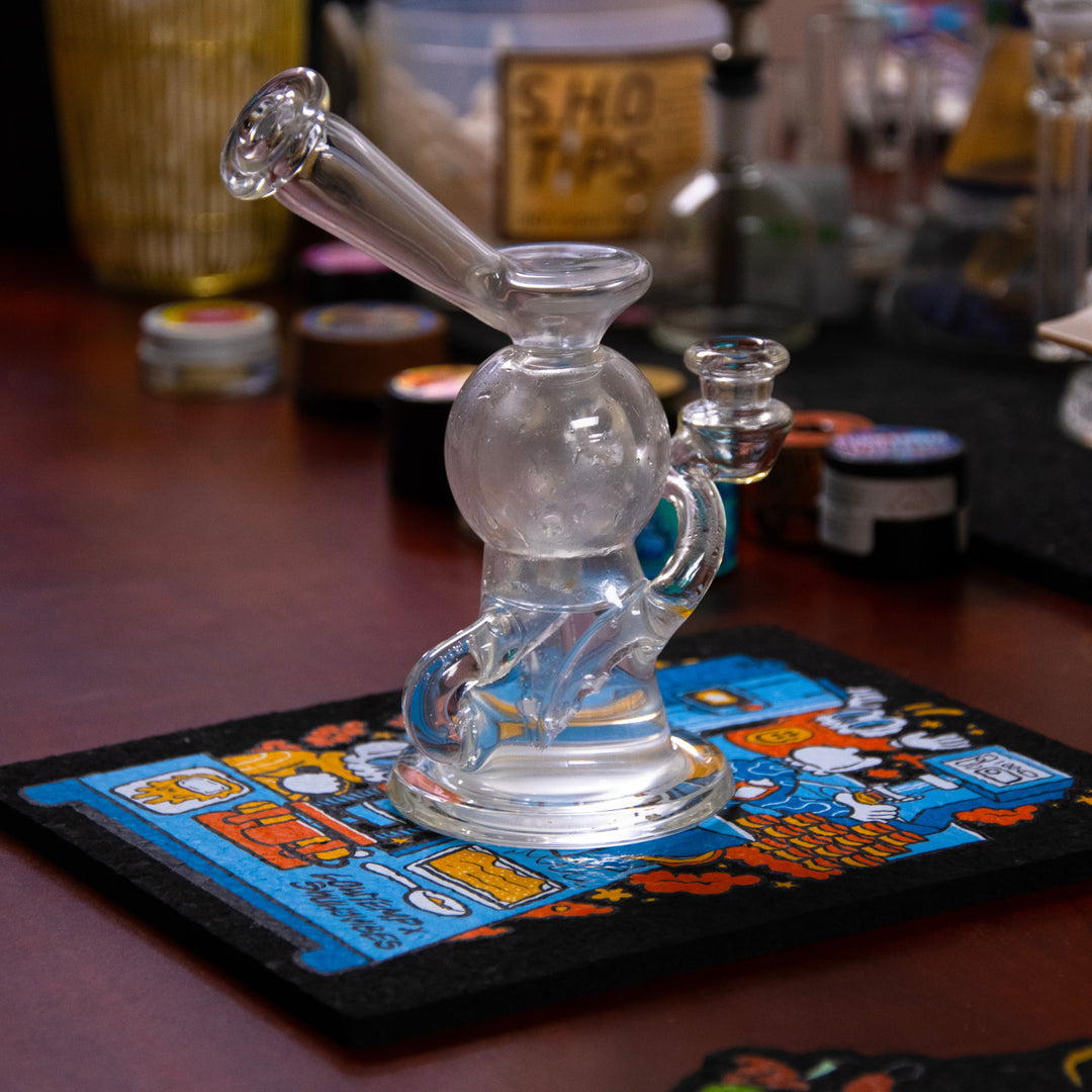 Clear glass smoking device on a colorful coaster with a blurred background