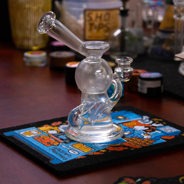Clear glass smoking device on a colorful coaster with a blurred background